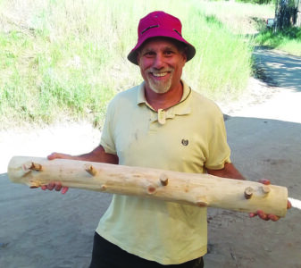 A person holds up a wooden coat rack they made and smiles at the